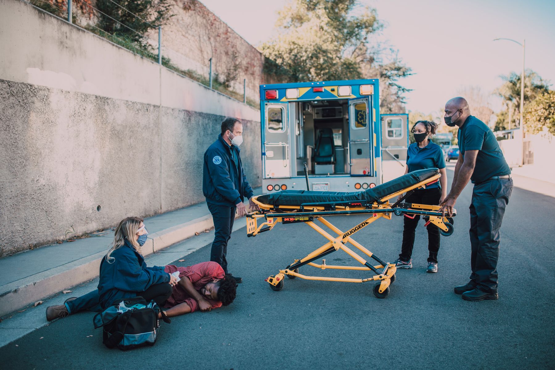 An EMS crew preparing a stretcher while a responder provides care at the scene